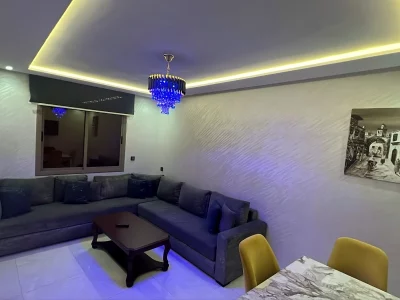 Salon avec canapé d'angle, lustre bleu et éclairage LED d'ambiance - Appart'Hôtel Nador De Luxe