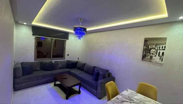 Salon avec canapé d'angle, lustre bleu et éclairage LED d'ambiance - Appart'Hôtel Nador De Luxe