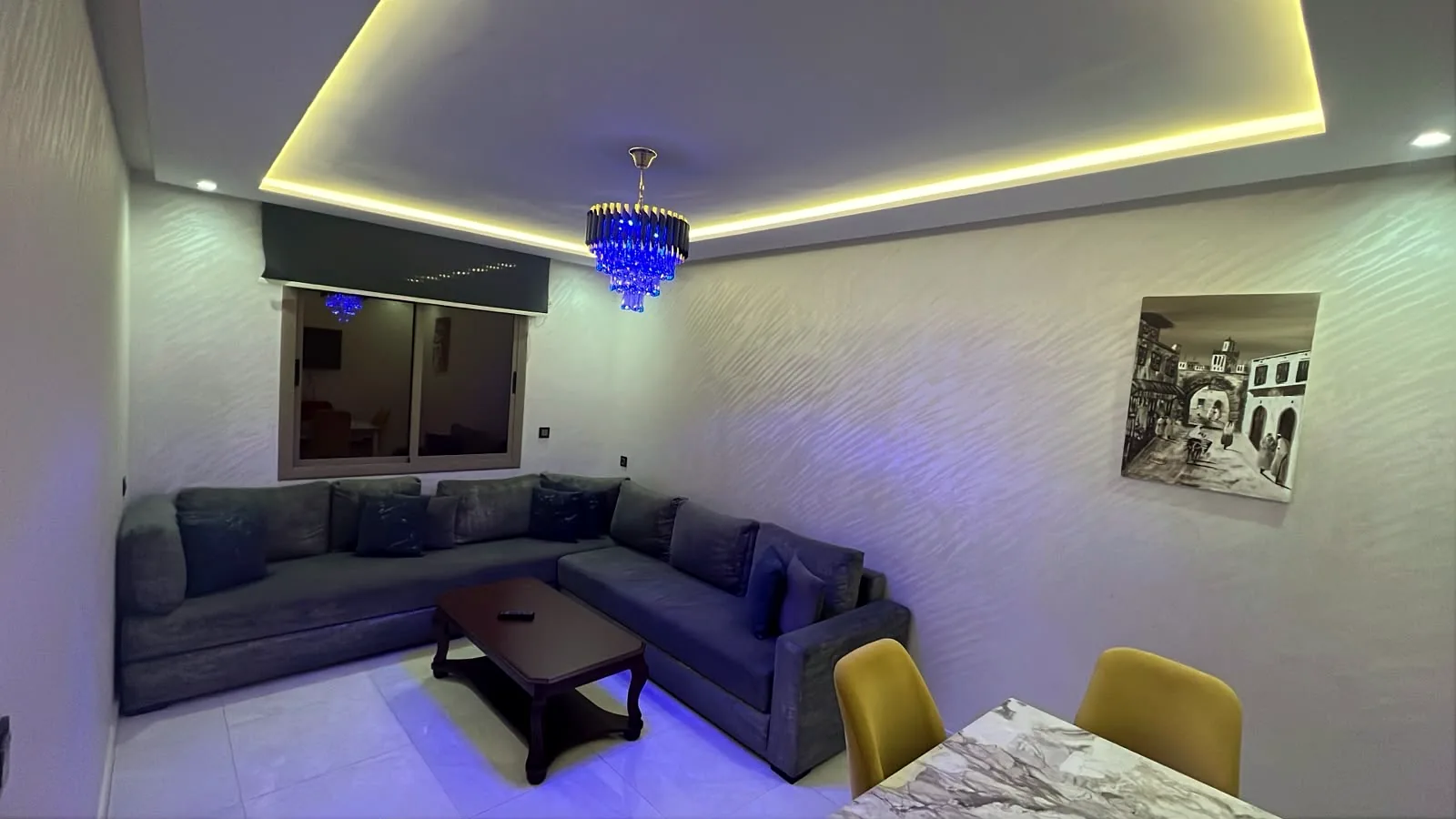 Salon avec canapé d'angle, lustre bleu et éclairage LED d'ambiance - Appart'Hôtel Nador De Luxe