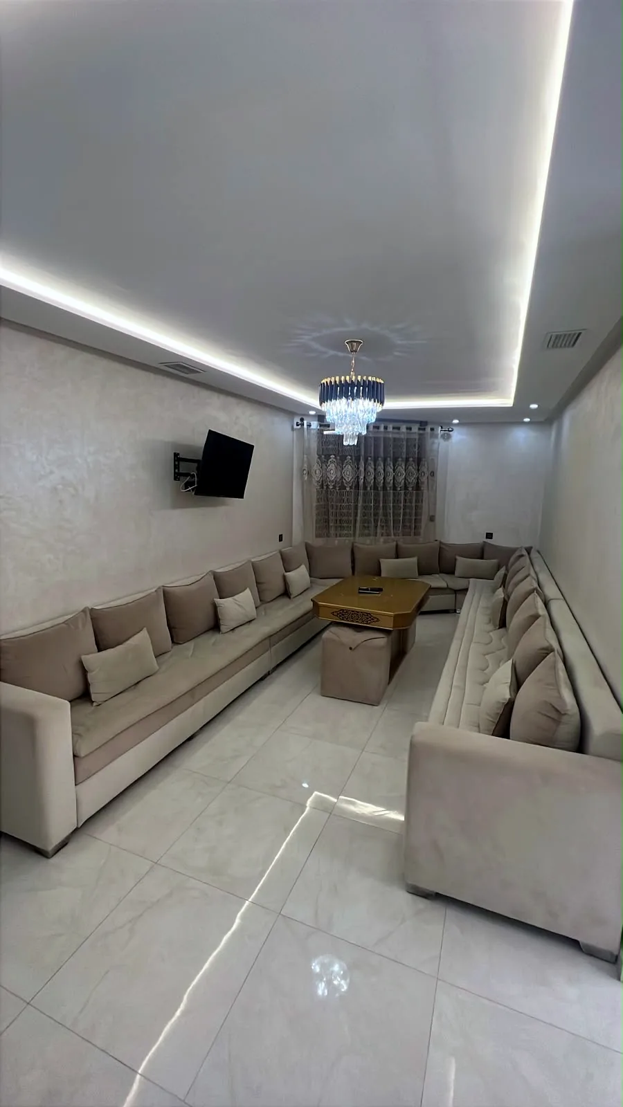 Grand salon marocain avec téléviseur, lustre en cristal et éclairage LED - Appart'Hôtel Nador De Luxe